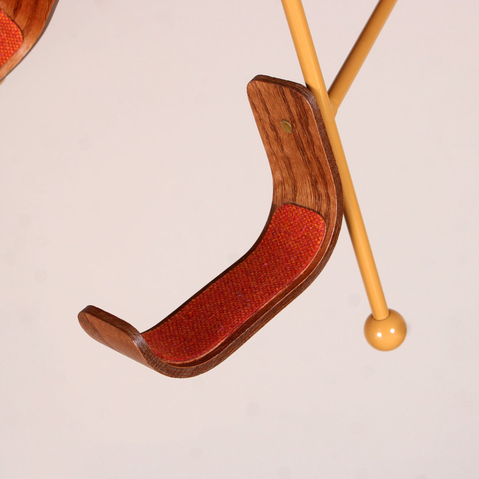 Close-up of VHS Edition Guitar Stand with stained oak rest and orange tweed padding on a cream powder-coated steel frame.