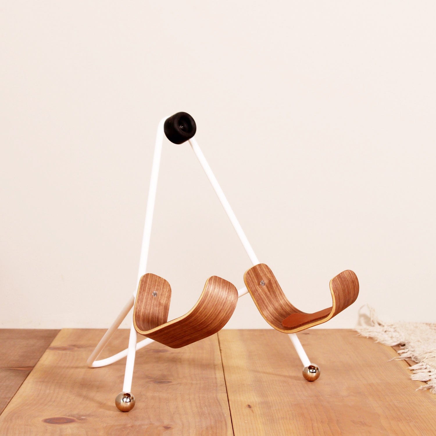 A angled front view of a white painted metal guitar stand with wooden guitar body rests