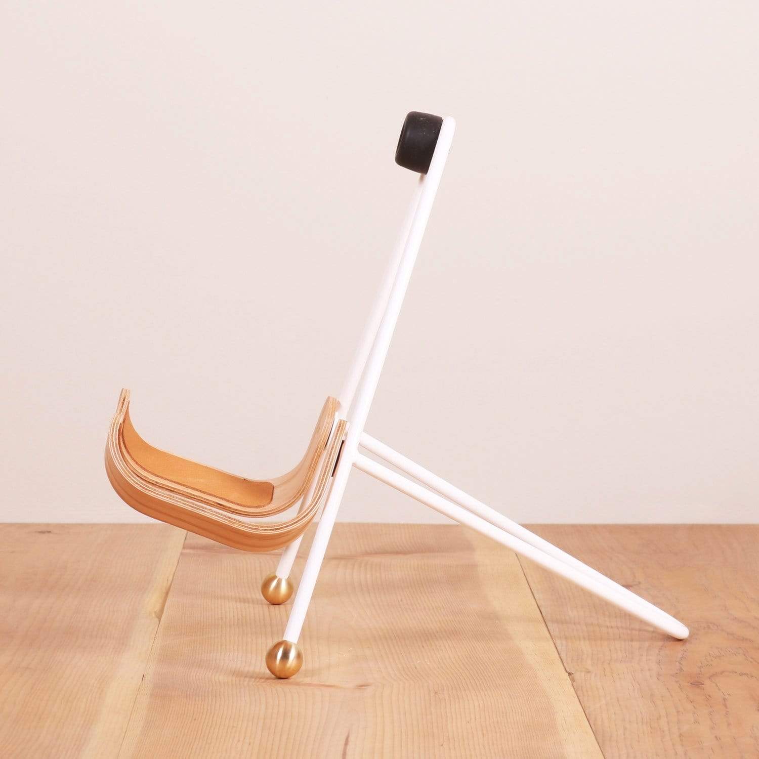 A sideview of a white guitar stand with wooden guitar body rests 