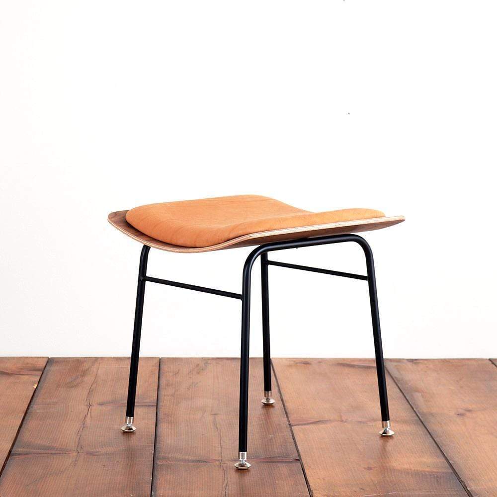 A mid-century modern style chair with a black metal frame and tan leather seat, placed on a wooden floor against a plain white background.